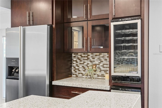 kitchen with tasteful backsplash, wine cooler, dark brown cabinetry, stainless steel refrigerator with ice dispenser, and light stone countertops