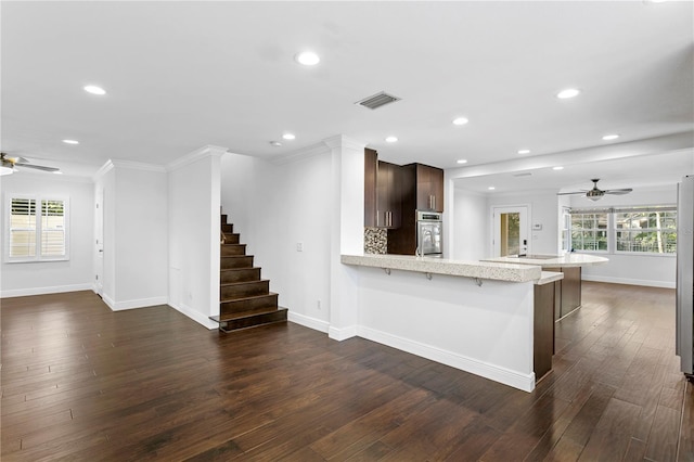 kitchen with a breakfast bar area, dark hardwood / wood-style flooring, ceiling fan, kitchen peninsula, and dark brown cabinets