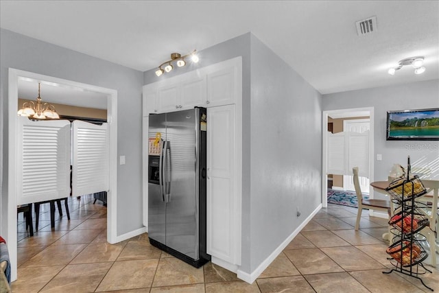 kitchen featuring stainless steel refrigerator with ice dispenser, white cabinetry, a notable chandelier, and light tile patterned floors