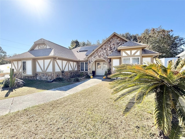 tudor-style house featuring french doors, a front yard, and solar panels