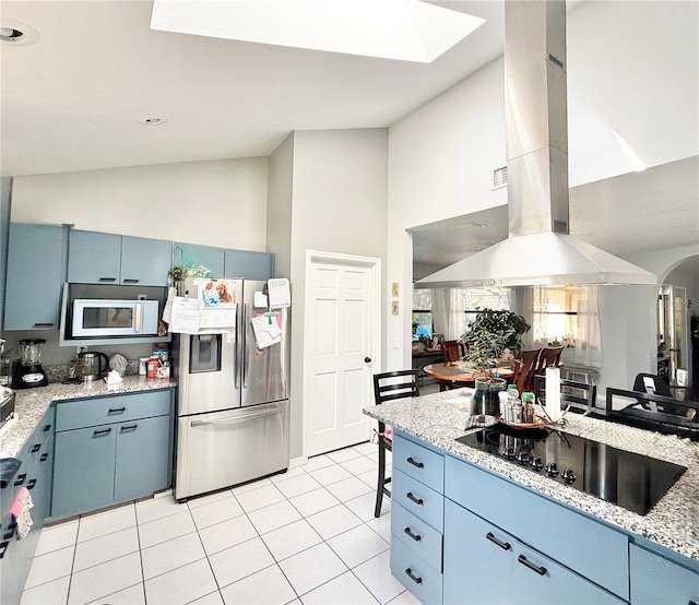 kitchen featuring stainless steel refrigerator with ice dispenser, blue cabinetry, lofted ceiling with skylight, island exhaust hood, and black electric stovetop