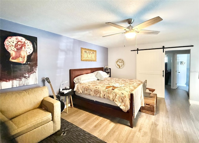 bedroom with ceiling fan, wood-type flooring, a barn door, and a textured ceiling