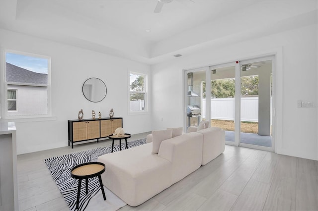 living room with light hardwood / wood-style flooring, plenty of natural light, a raised ceiling, and ceiling fan