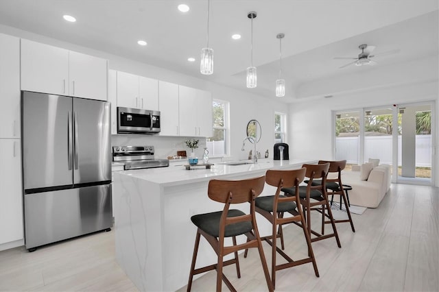 kitchen with sink, a breakfast bar, appliances with stainless steel finishes, white cabinetry, and an island with sink