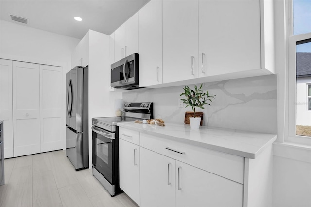 kitchen featuring white cabinetry, a healthy amount of sunlight, stainless steel appliances, and light stone counters