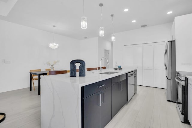 kitchen with sink, stainless steel appliances, decorative light fixtures, and an island with sink