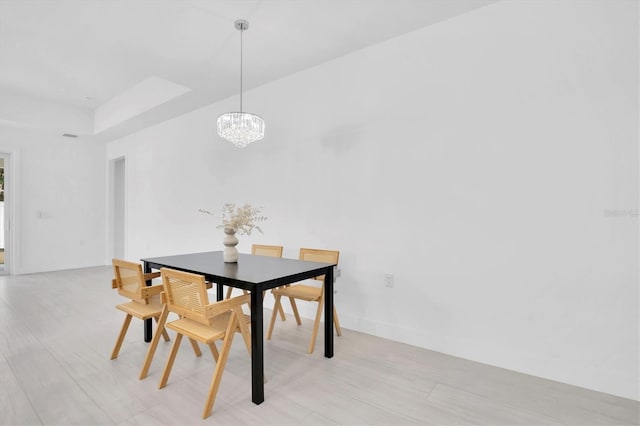 dining room with a raised ceiling, light wood-type flooring, and a chandelier