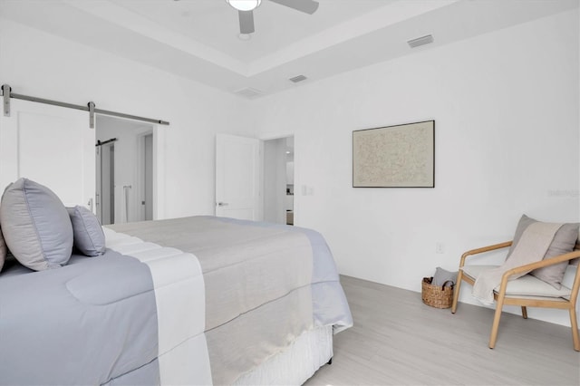 bedroom featuring ceiling fan, a barn door, a raised ceiling, and light wood-type flooring