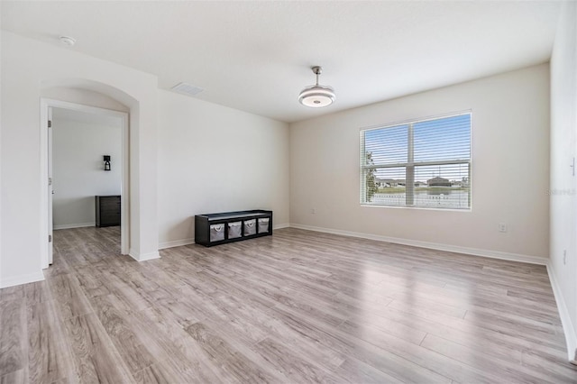 empty room with baseboards, light wood-style floors, visible vents, and arched walkways