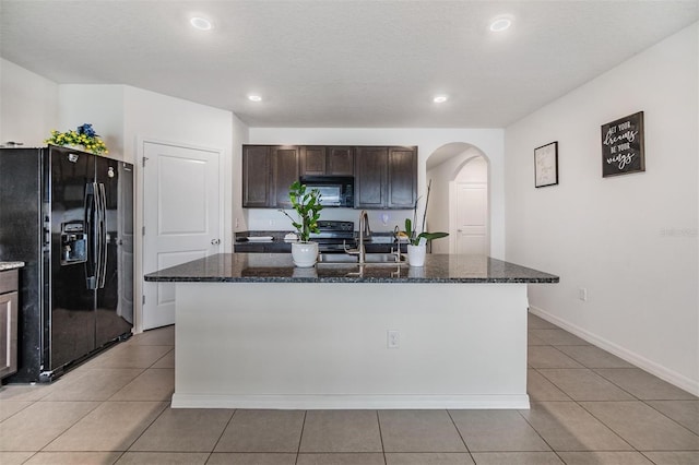 kitchen with a sink, dark stone counters, arched walkways, and black appliances