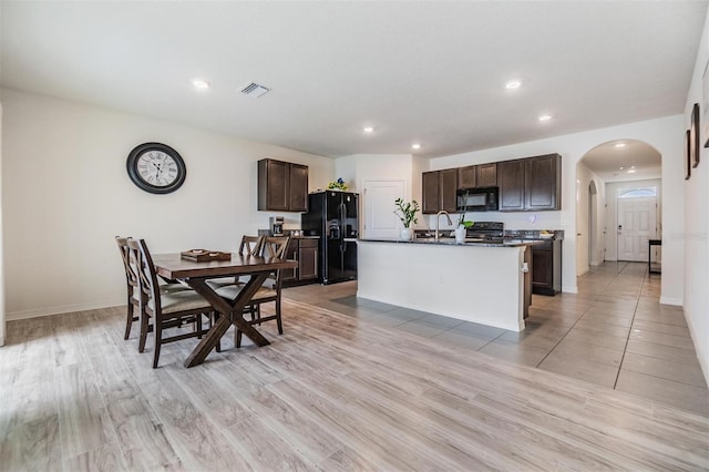 kitchen with visible vents, dark brown cabinets, arched walkways, black appliances, and a kitchen island with sink