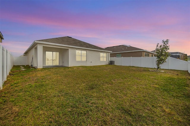 back of property featuring stucco siding, a fenced backyard, a yard, cooling unit, and a shingled roof