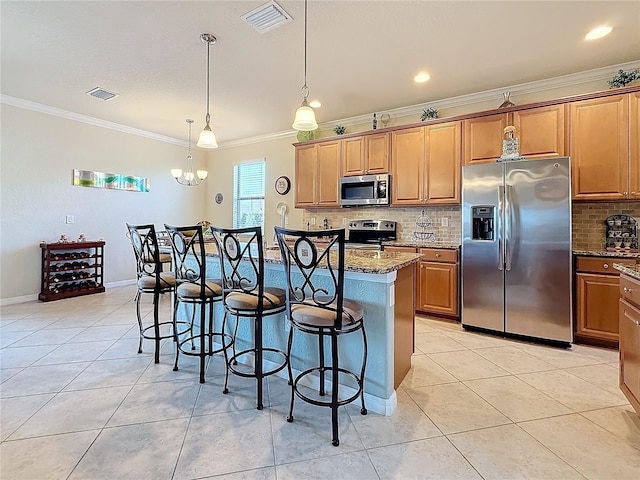 kitchen featuring crown molding, dark stone countertops, stainless steel appliances, an island with sink, and a kitchen bar