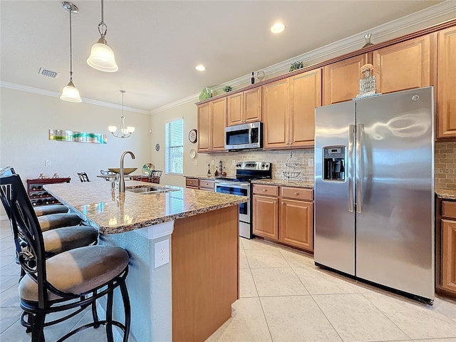 kitchen featuring sink, crown molding, stainless steel appliances, light stone counters, and an island with sink