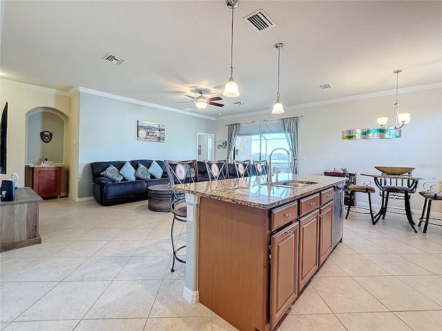 kitchen with a kitchen bar, sink, light stone counters, ornamental molding, and a kitchen island with sink