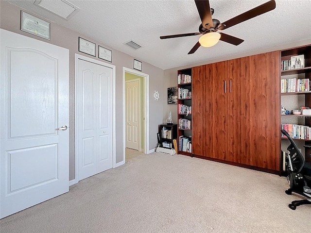 unfurnished office featuring ceiling fan, light carpet, and a textured ceiling