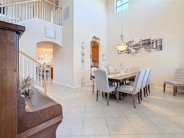 dining room with a towering ceiling, stairway, baseboards, arched walkways, and light tile patterned floors
