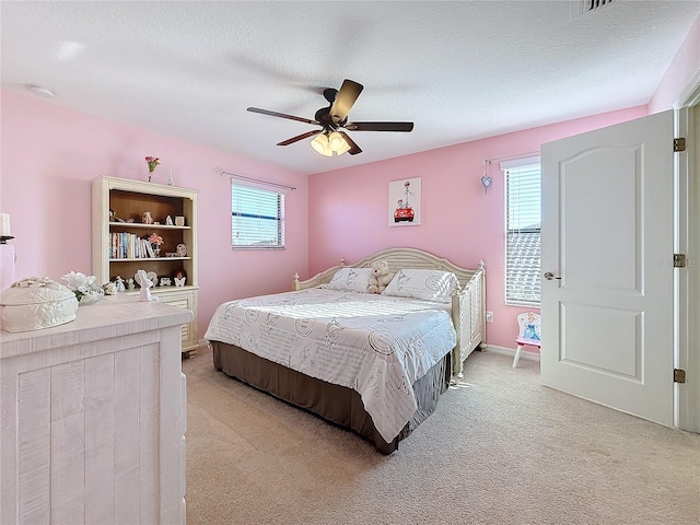 bedroom with light colored carpet, ceiling fan, and a textured ceiling