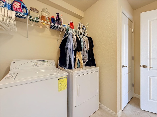 clothes washing area featuring washing machine and clothes dryer, light tile patterned floors, and baseboards