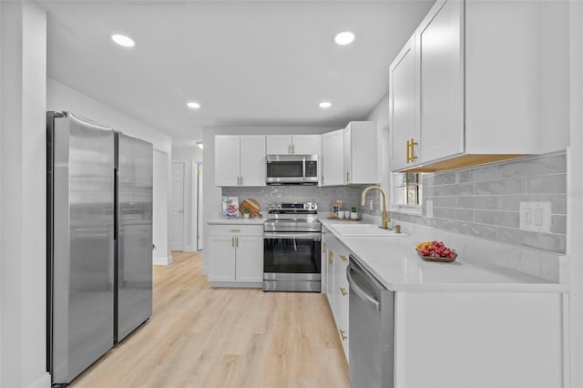 kitchen featuring sink, backsplash, stainless steel appliances, white cabinets, and light wood-type flooring