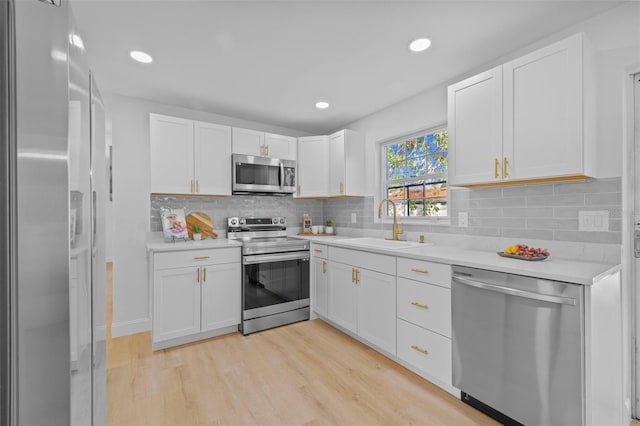 kitchen featuring sink, appliances with stainless steel finishes, white cabinetry, backsplash, and light wood-type flooring