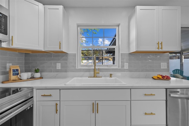 kitchen featuring appliances with stainless steel finishes, tasteful backsplash, white cabinetry, sink, and light stone countertops