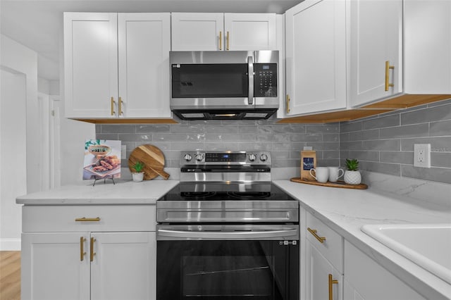 kitchen with appliances with stainless steel finishes, white cabinets, decorative backsplash, light stone countertops, and light hardwood / wood-style flooring