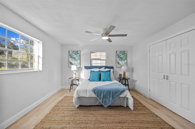 bedroom with ceiling fan, a closet, light hardwood / wood-style floors, and multiple windows