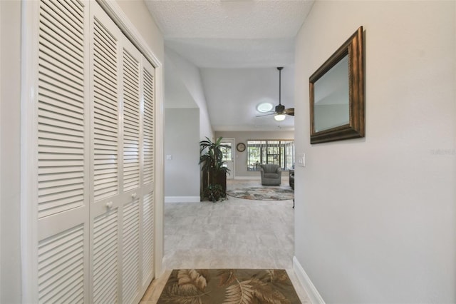 corridor with lofted ceiling, a textured ceiling, and light hardwood / wood-style floors