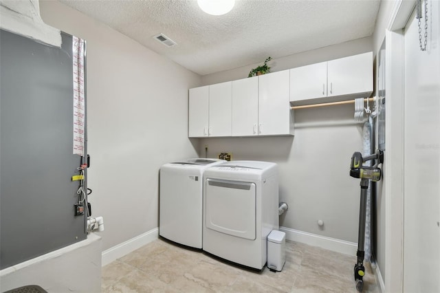 clothes washing area with washing machine and dryer, cabinets, and a textured ceiling