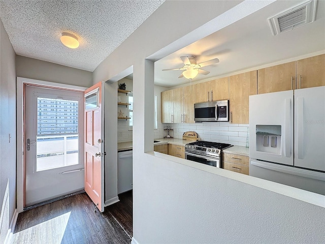 kitchen with light brown cabinetry, a textured ceiling, dark hardwood / wood-style flooring, stainless steel appliances, and backsplash