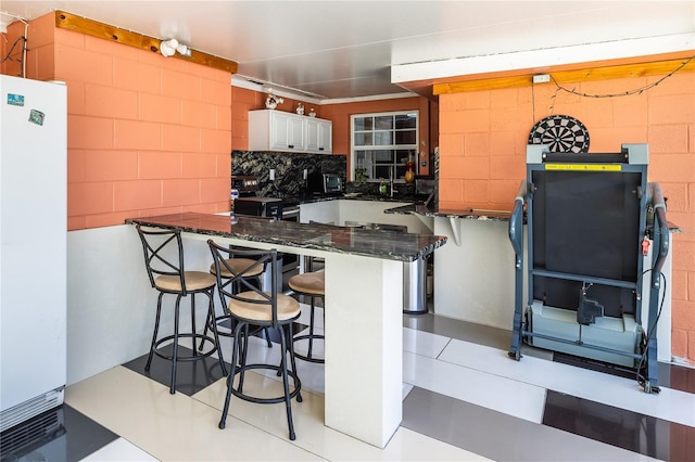 kitchen with a breakfast bar, white cabinetry, dark stone countertops, white fridge, and kitchen peninsula