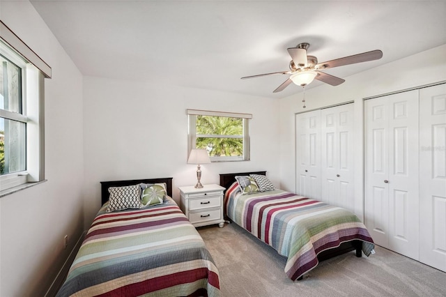 bedroom with two closets, light carpet, and ceiling fan