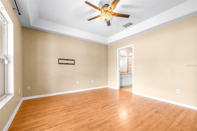 empty room with ceiling fan, a tray ceiling, and light wood-type flooring