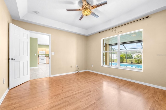 empty room featuring ceiling fan, a raised ceiling, and light hardwood / wood-style flooring