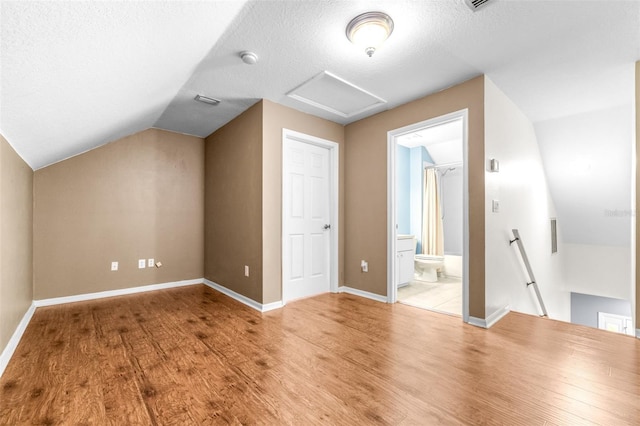 bonus room with lofted ceiling, light hardwood / wood-style floors, and a textured ceiling