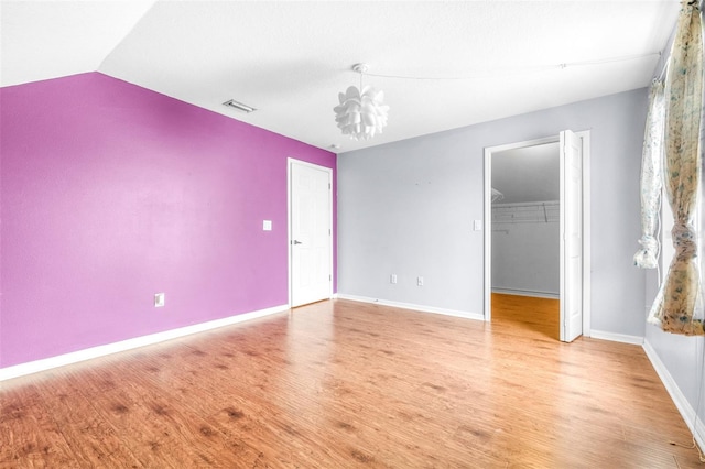 unfurnished bedroom with lofted ceiling, a spacious closet, a chandelier, light wood-type flooring, and a closet