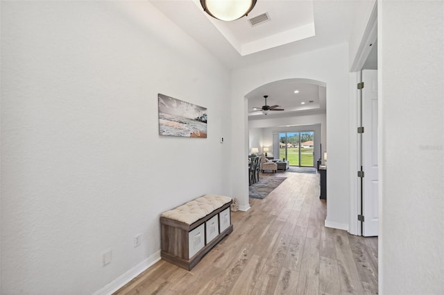 hall with a tray ceiling and light wood-type flooring