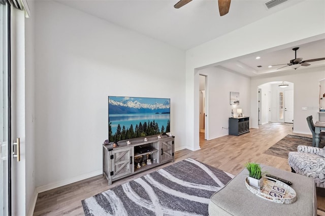 living room with hardwood / wood-style flooring, a raised ceiling, and ceiling fan