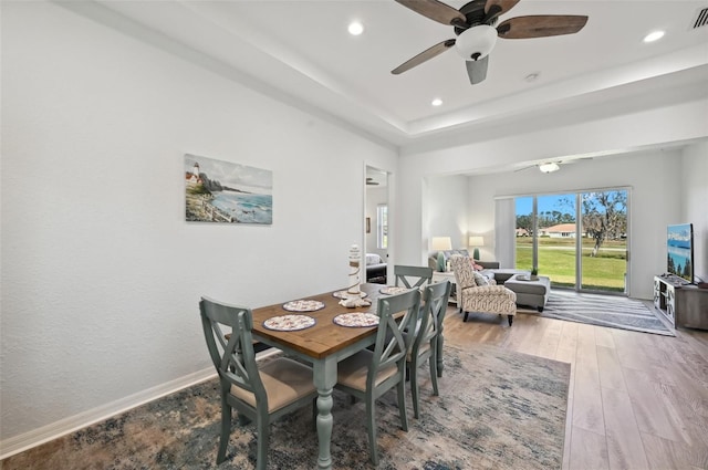 dining space with ceiling fan, a tray ceiling, and hardwood / wood-style floors