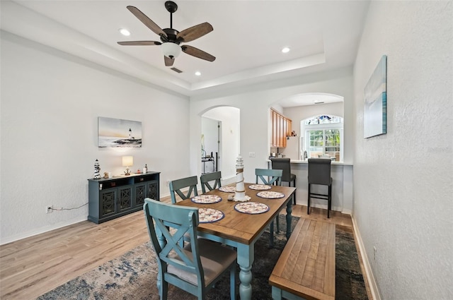 dining space with light hardwood / wood-style flooring, ceiling fan, and a tray ceiling