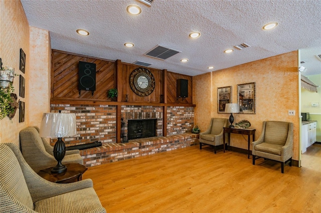 living area with a fireplace, wood finished floors, visible vents, and a textured ceiling