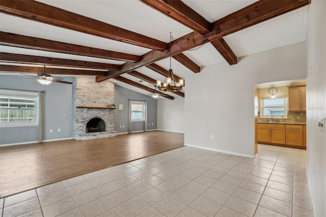 unfurnished living room with sink, a fireplace, lofted ceiling with beams, light tile patterned flooring, and ceiling fan with notable chandelier