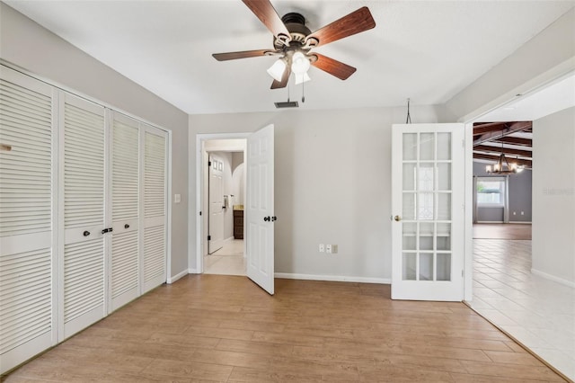 unfurnished bedroom with ceiling fan with notable chandelier, light wood-type flooring, and french doors