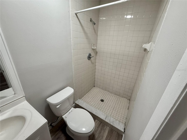 bathroom with wood-type flooring, toilet, vanity, and a tile shower