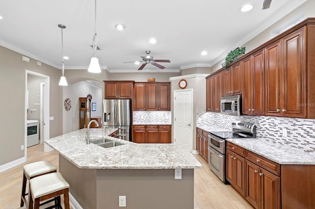 kitchen featuring sink, hanging light fixtures, stainless steel appliances, a center island with sink, and light hardwood / wood-style flooring