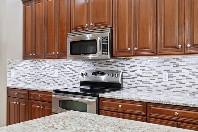 kitchen with light stone counters, stainless steel appliances, and backsplash