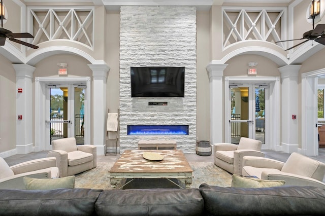 living room with french doors, ceiling fan, a stone fireplace, and a towering ceiling