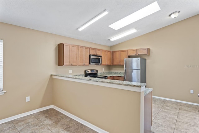 kitchen featuring light stone counters, appliances with stainless steel finishes, vaulted ceiling with skylight, and kitchen peninsula