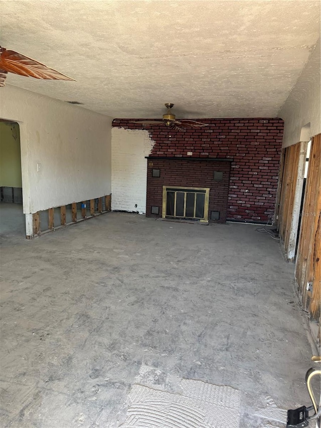 unfurnished living room featuring ceiling fan, a textured ceiling, and a fireplace